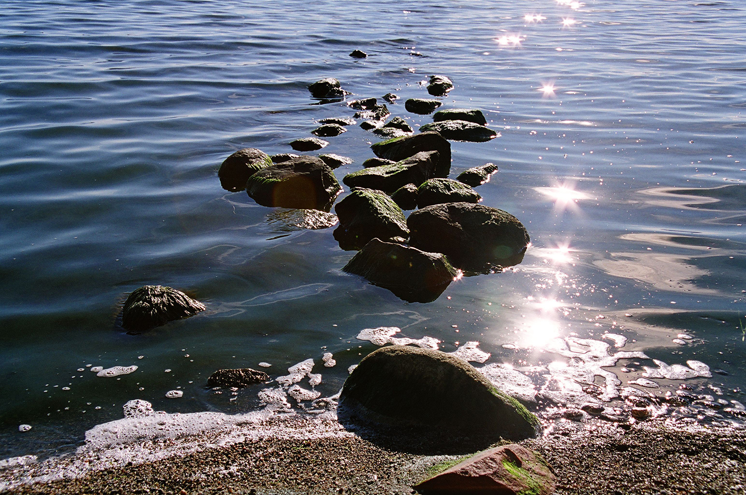 Aurinko kisailee rannan kivien lomassa