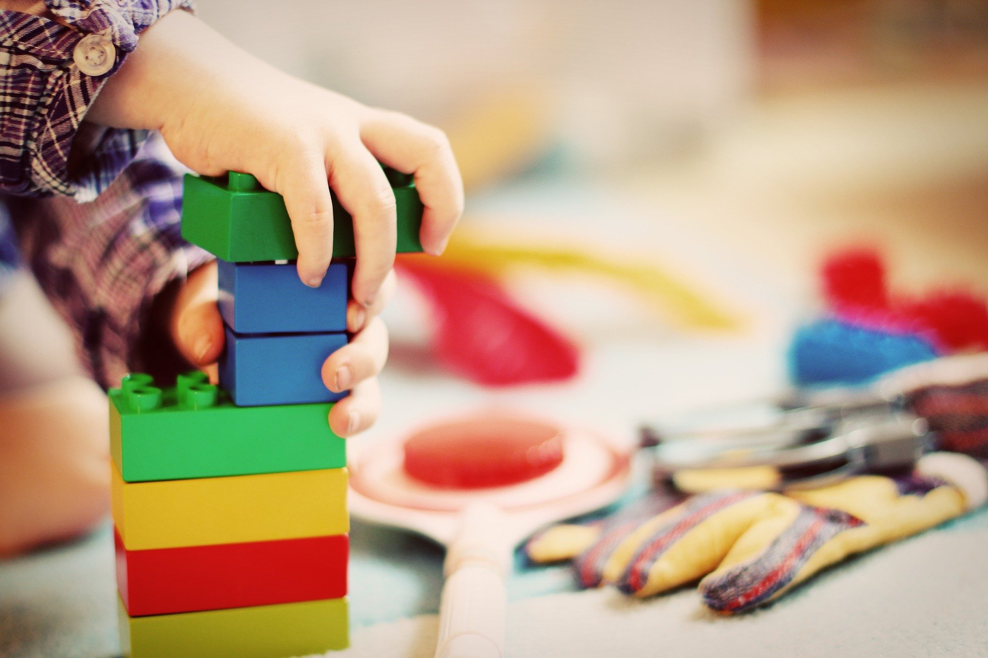 Lapsen kädet, lego-palikoista tehty torni ja leluja.