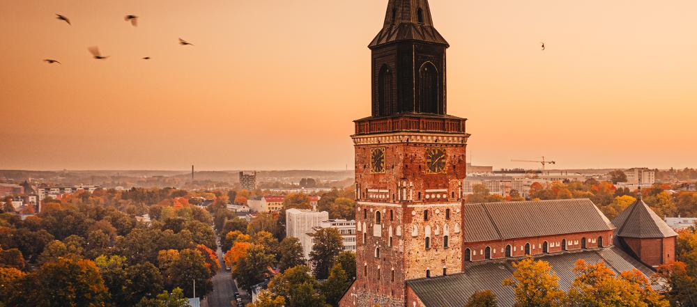 Turku Cathedral in autumn, tower against an orange sky, some birds flying by