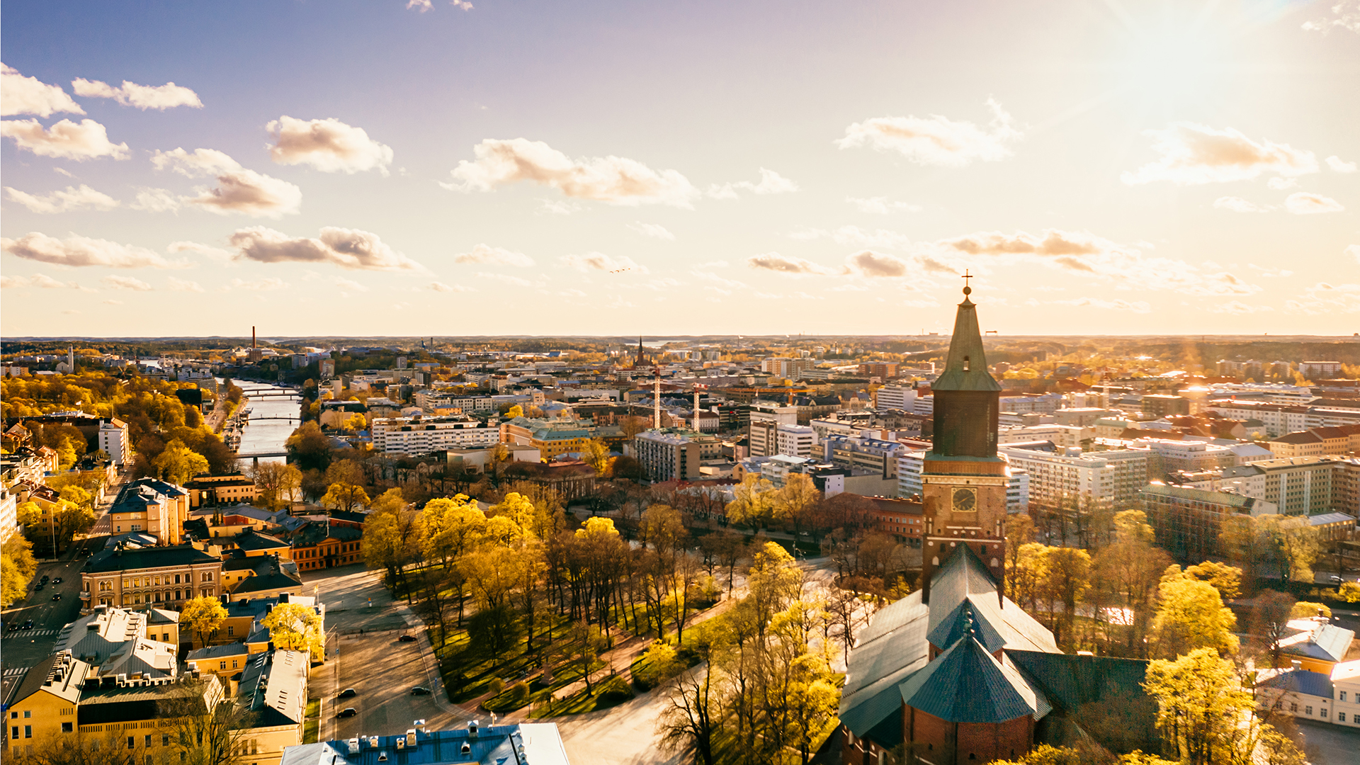 Ilmakuva Tuomiokirkosta kaupunkimaisemassa. Puut hiirekorvalla, aurinko paistaa